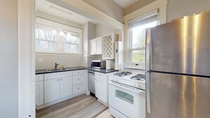 Une cuisine avec des meubles blancs, un réfrigérateur en acier inoxydable, un four à micro-ondes, une cuisinière à gaz et un lave-vaisselle.