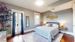 Une chambre à coucher avec un lit, des tables de chevet, un miroir et une fenêtre.