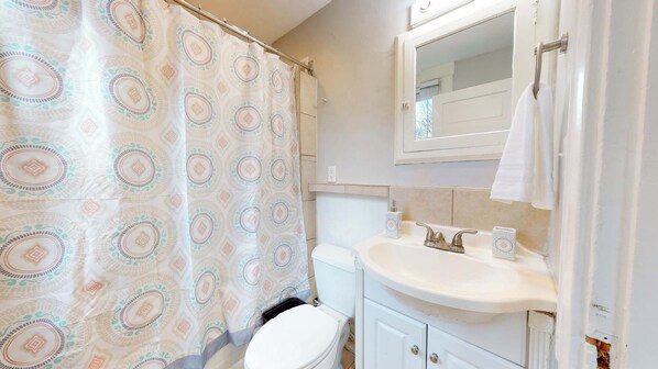 A bathroom with a shower curtain, a toilet, a sink with a mirror above it, and a towel hanging on the wall. - Vista View Villa Suites – 2 Private Condos! (Cincinnati)