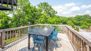 Een houten terras met een tafel en stoelen, omringd door een houten balustrade, met uitzicht op een weelderig groonlandschap.