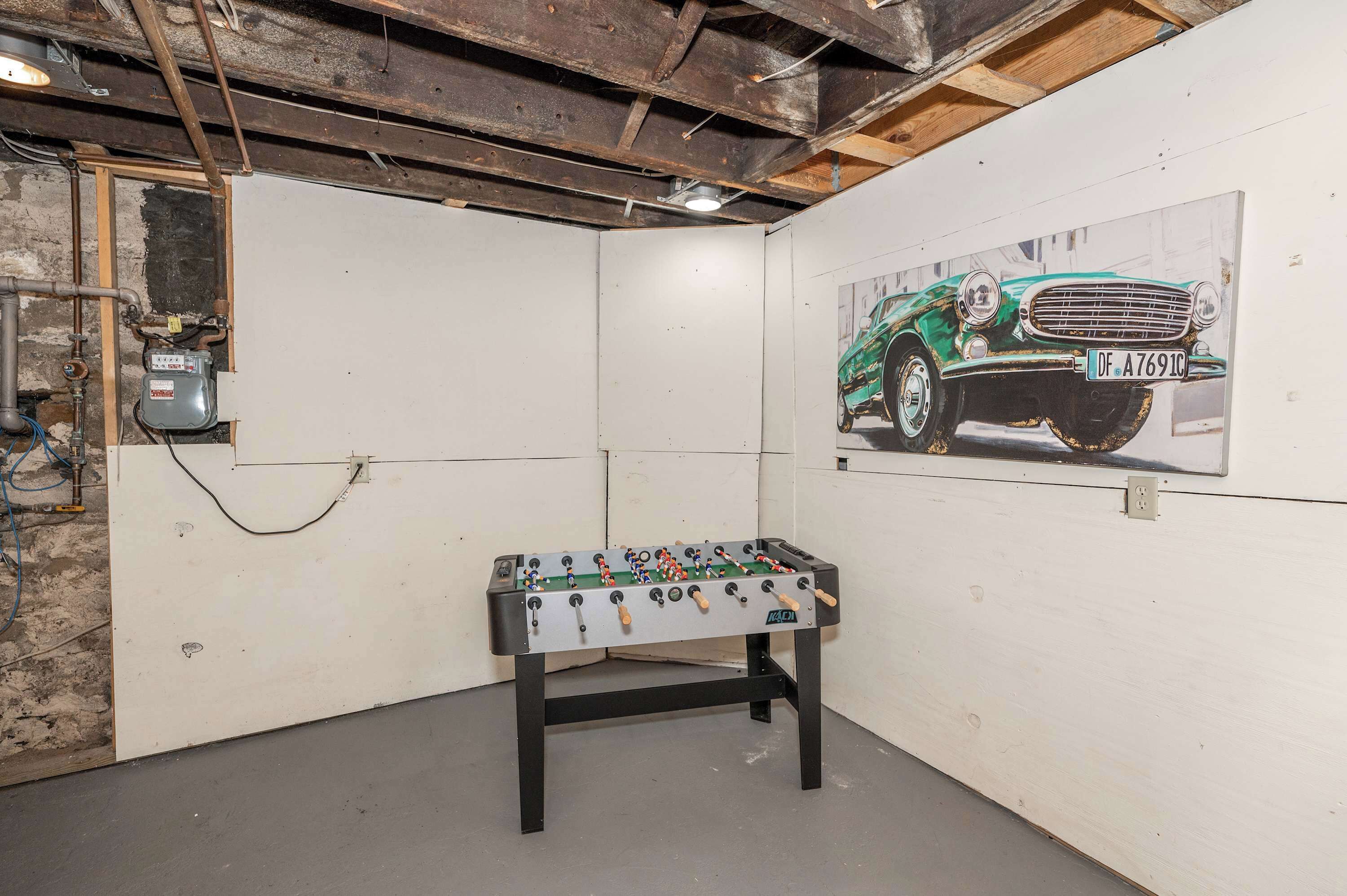 Una habitación con mesa de futbolín, un cartel de coche clásico y vigas de techo a la vista.