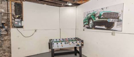Una habitación con mesa de futbolín, un cartel de coche clásico y vigas de techo a la vista.