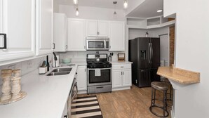 Una cocina moderna con armarios blancos, electrodomésticos de acero inoxidable e iluminación colgante.