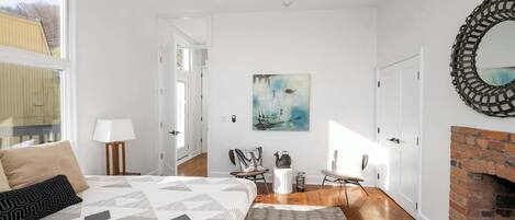 Un dormitorio con cama, chimenea, un cuadro y vistas al exterior.