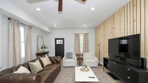 A living room with a brown leather sofa, a white armchair, a coffee table, a TV, and a wooden wall panel.