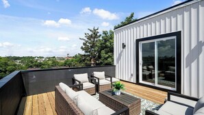 A rooftop patio with wicker furniture, a wooden deck, and a sliding glass door leading to an outdoor seating area.