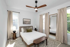 A bedroom with a bed, bedside tables, a ceiling fan, a window with curtains, and a view of greenery outside. - Heights on Wayne by Blackhouse (Cincinnati)