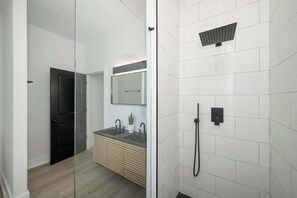 A modern bathroom with a glass shower enclosure, a black door, a wooden vanity, and a white tiled wall. - Heights on Wayne by Blackhouse (Cincinnati)