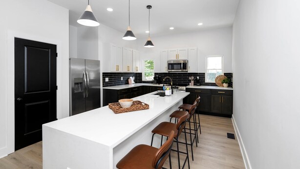 A modern kitchen with a central island, black cabinets, stainless steel appliances, and pendant lighting.