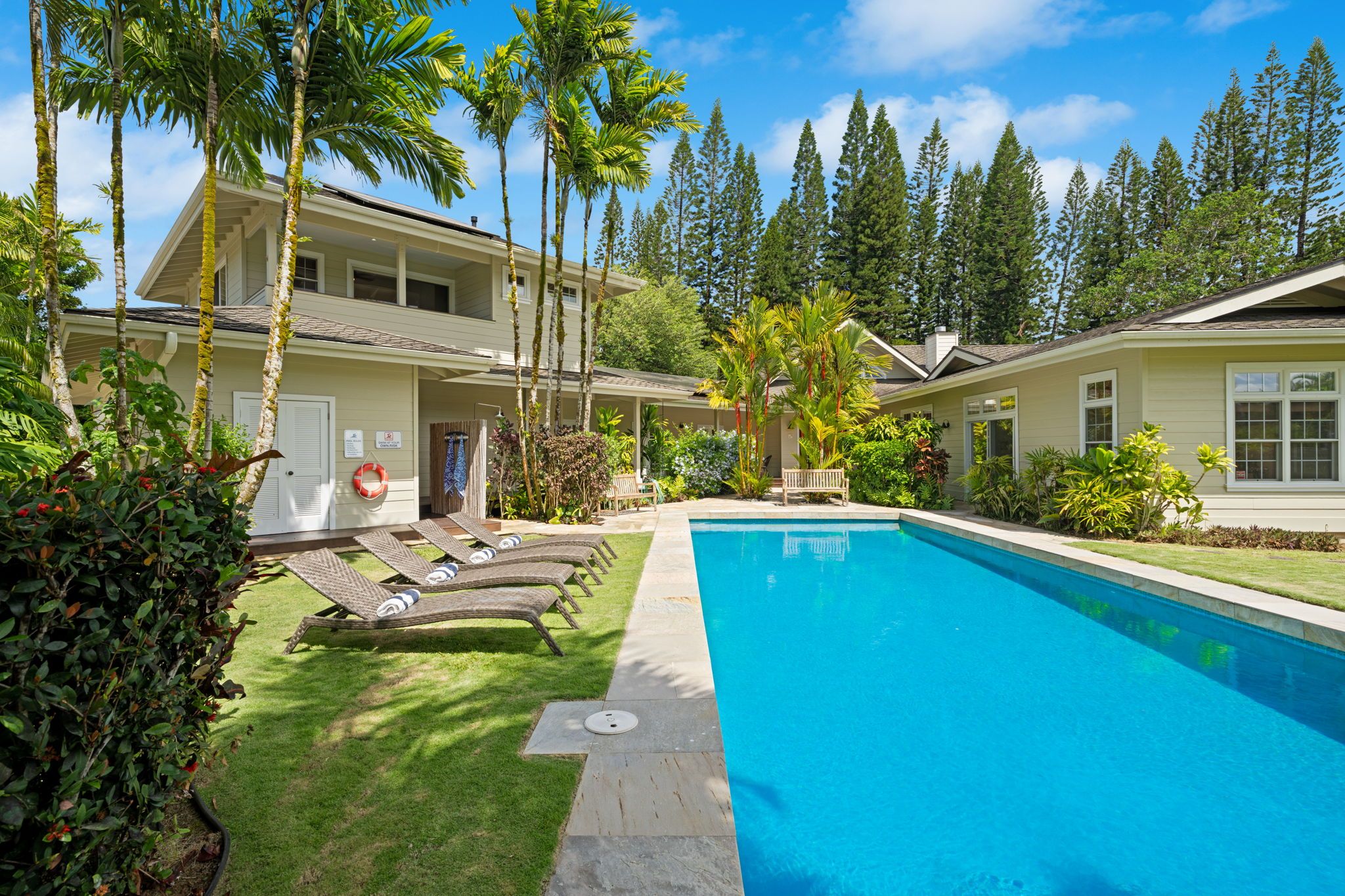 A two-story house with a swimming pool, surrounded by palm trees and a well-maintained lawn.
