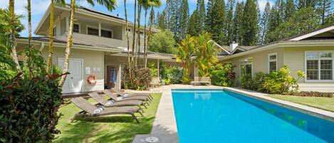 A two-story house with a swimming pool, surrounded by palm trees and a well-maintained lawn.