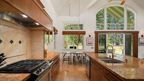 A kitchen with a large island, double sink, and a dining area with a view of the outdoors. - Lei Aloha - A Private Retreat, Pool + Fairway views (Princeville)