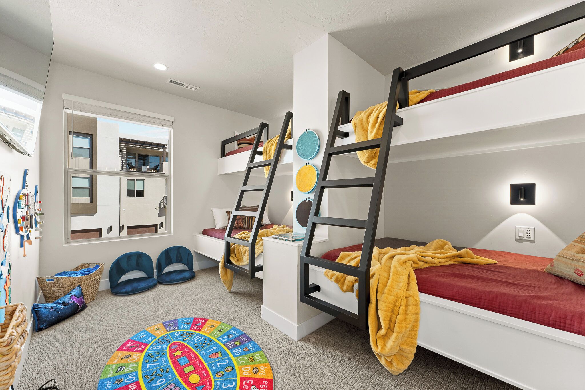 Camera da letto per bambini con letti a castello, angolo giochi e finestra vista su un edificio.