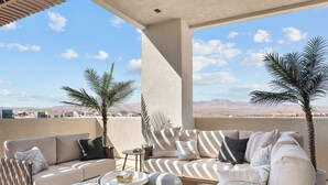 Eine Dachterrasse mit einem beigefarbenen Sofa, gestreiften Kissen und zwei Palmen.