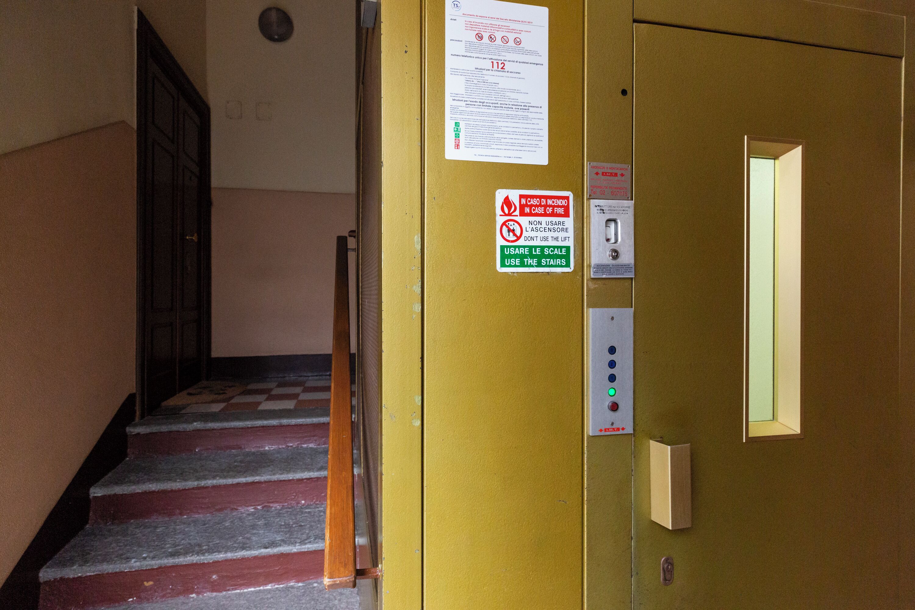 A staircase leading to an elevator with safety signs and a fire emergency exit sign.