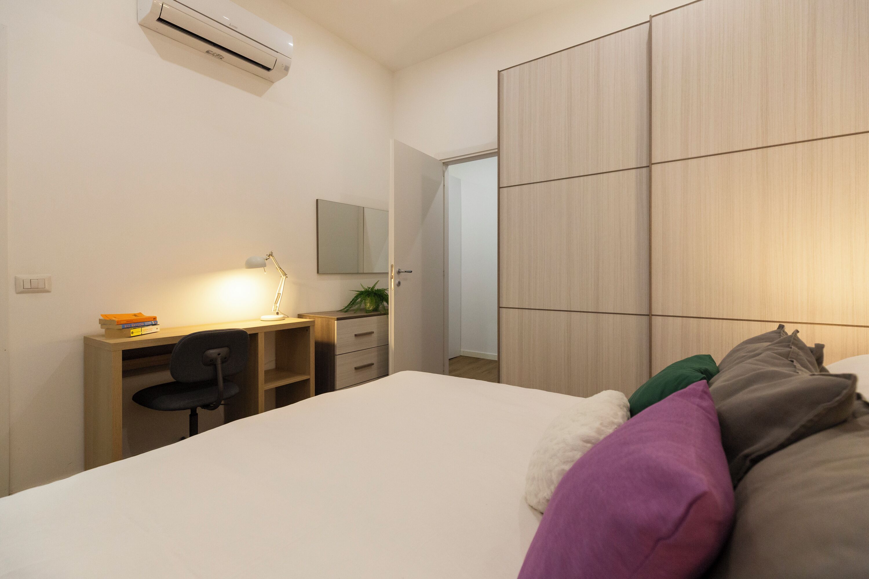 Une chambre à coucher avec un lit, un bureau avec une chaise, un miroir et une armoire.