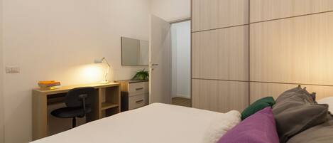Une chambre à coucher avec un lit, un bureau avec une chaise, un miroir et une armoire.