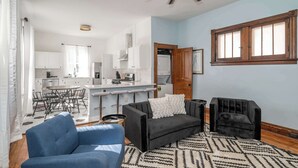Eine moderne Küche mit weißen Schränken, ein Essbereich mit rundem Tisch und Stühlen, ein schwarzes Sofa und ein Deckenventilator.
