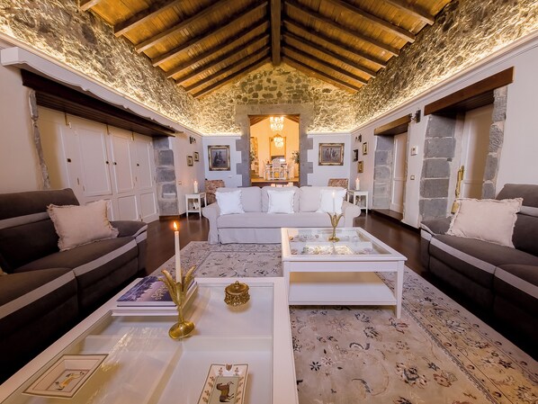A cozy living room with a stone wall, wooden ceiling beams, and a central chandelier.