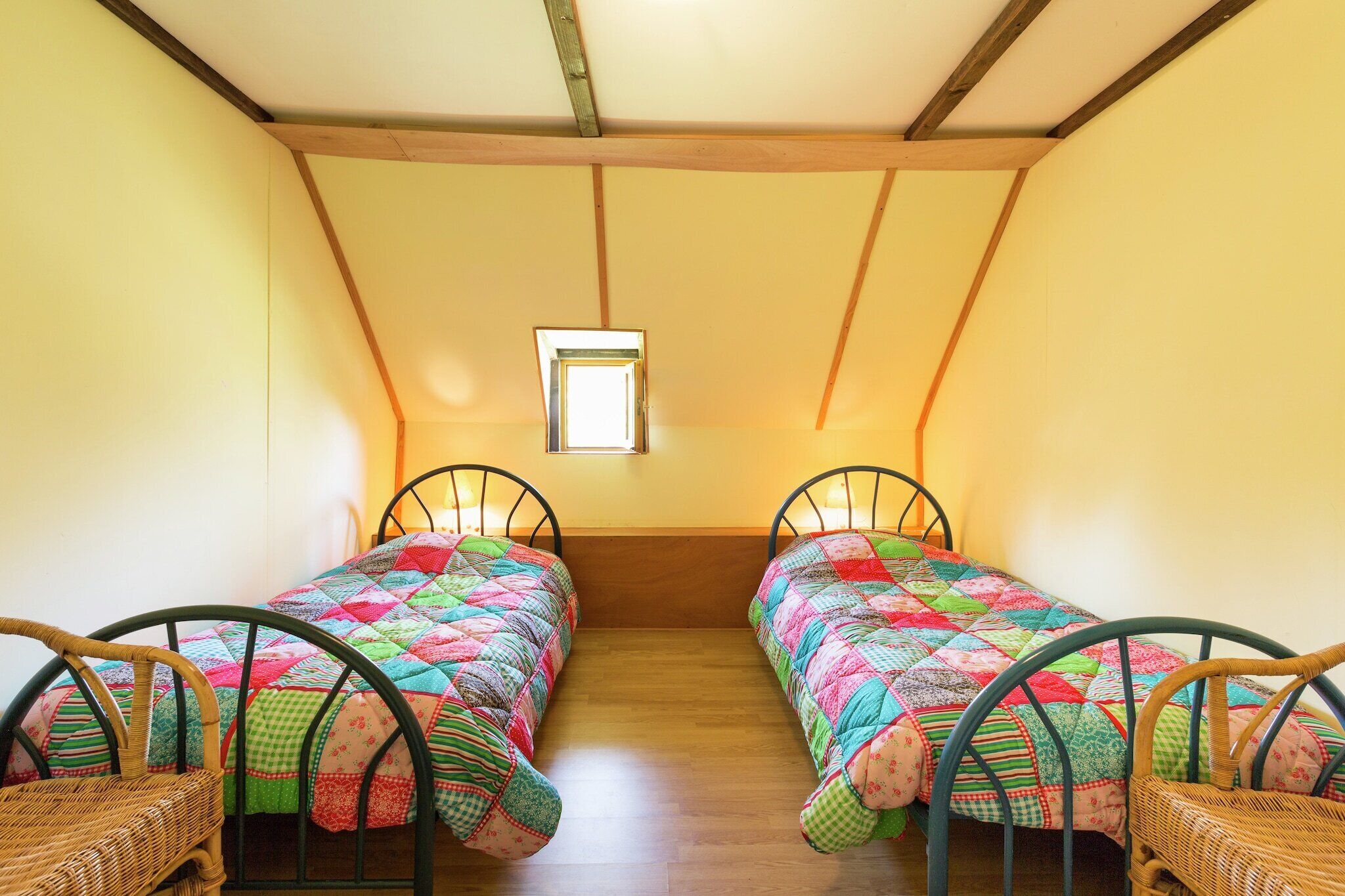 A small room with two single beds, wooden flooring, a window, and a sloped ceiling.