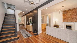 A spacious living area with a wooden staircase, a fireplace, and a modern chandelier. - Woodburn Villa by Blackhouse (Cincinnati)
