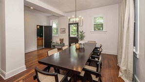 A dining room with a long table, chairs, a chandelier, and a potted plant. - Woodburn Villa by Blackhouse (Cincinnati)