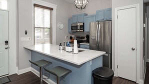 A modern kitchen with blue cabinets, a stainless steel refrigerator, a microwave, and a large island with bar stools. - Heart of Mainstrasse 3 (Covington)