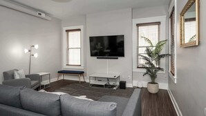 A modern living room with a grey sofa, a TV on the wall, a small side table, and a potted plant. - Heart of Mainstrasse 3 (Covington)