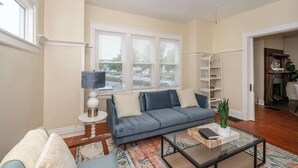 A living room with a sofa, a coffee table, and a bookshelf. - The Mariemont Cottage (Cincinnati)