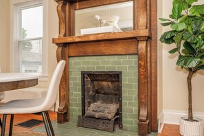 Une cheminée avec un encadrement en briques vertes, une cheminée en bois et une chaise blanche placée devant.