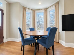 A dining area with a round table, four chairs, and large windows with curtains. - Near Cincy | Skyline Views | Historic 4BR (Ludlow)