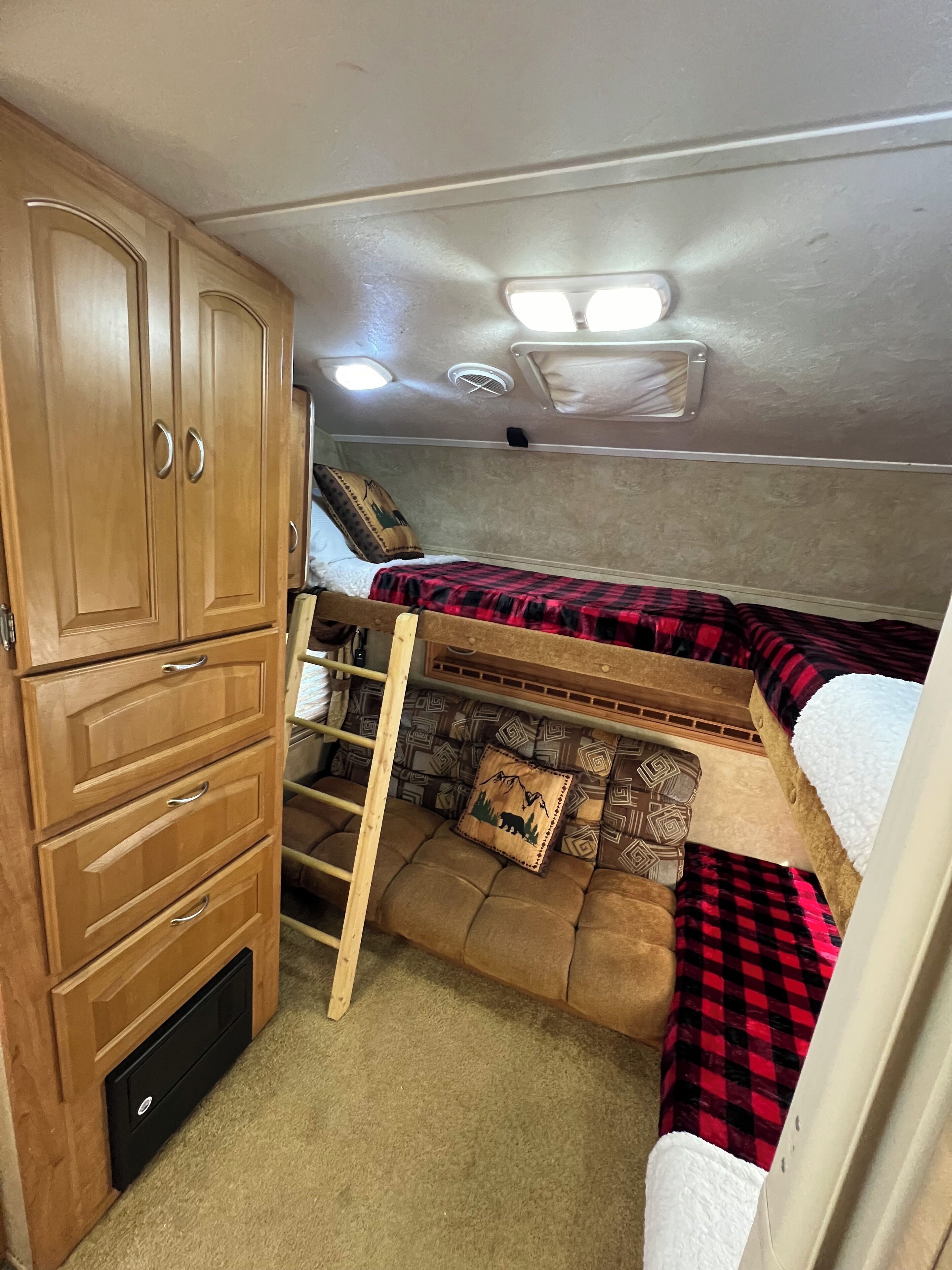 A compact RV interior with a bunk bed, wooden cabinets, and a small storage unit.