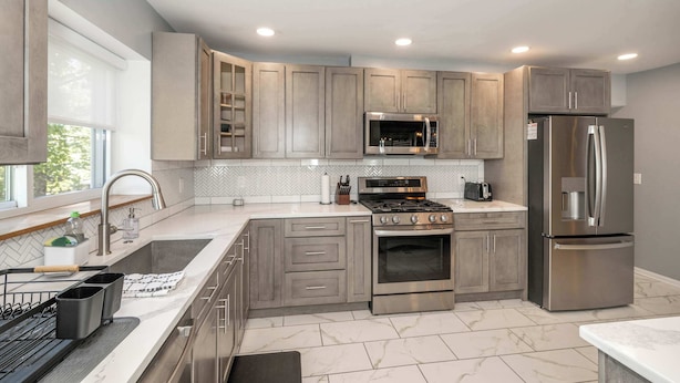 A modern kitchen with grey cabinets, stainless steel appliances, and a herringbone tile backsplash.