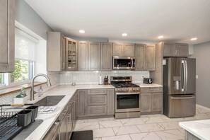 A modern kitchen with grey cabinets, stainless steel appliances, and a herringbone tile backsplash.
