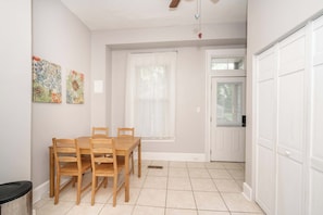 A dining area with a wooden table and chairs, a window with blinds, and a white door.
