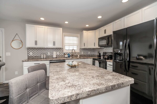 A modern kitchen with white cabinets, a granite countertop, a stainless steel refrigerator, and a microwave.