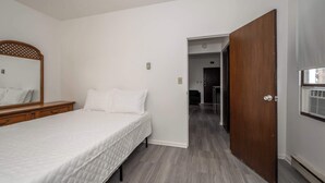 Een slaapkamer met een bed, een houten dressoir, een spiegel en een deur die uitkomt op een hal.
