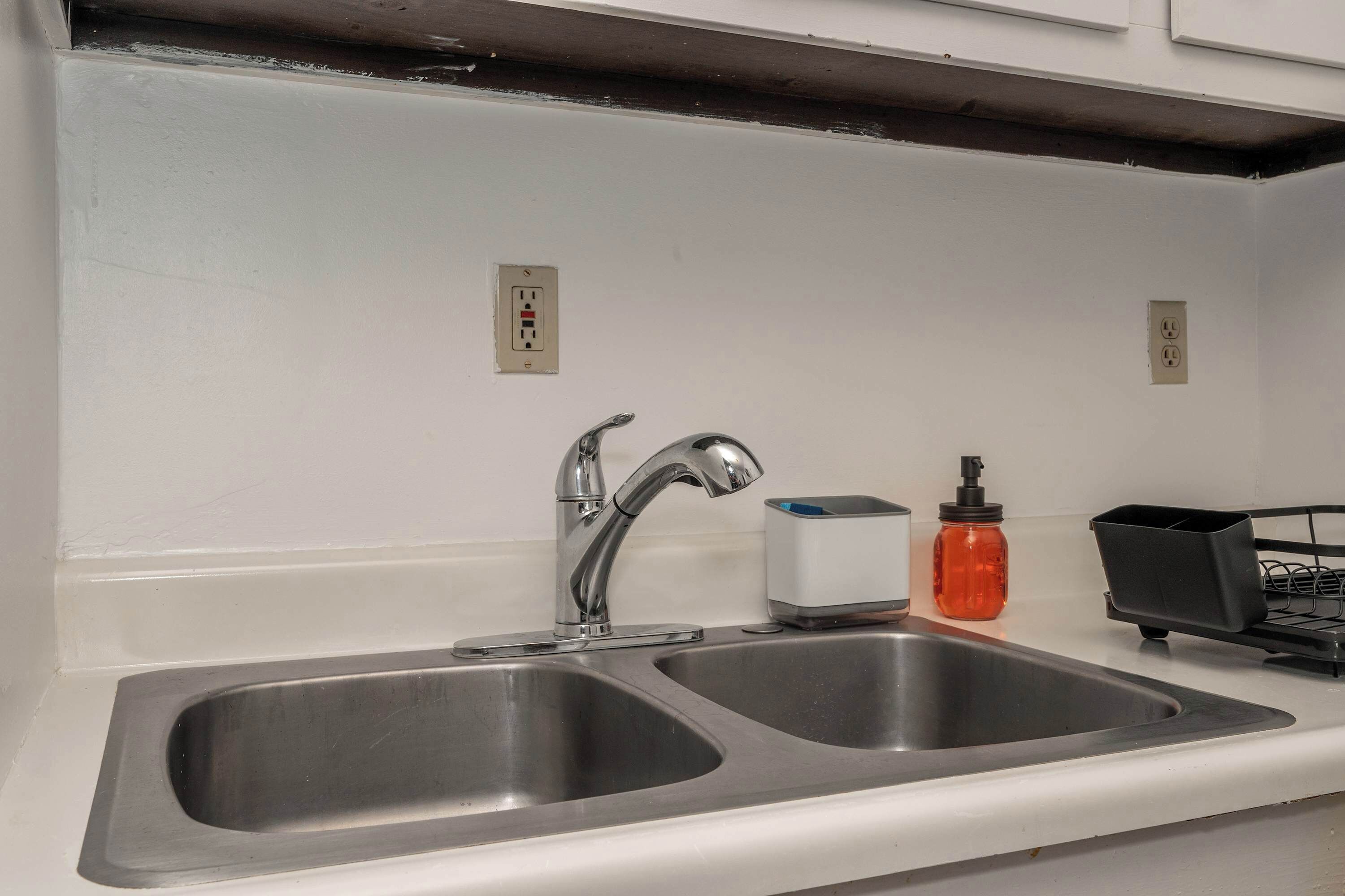 A kitchen with two stainless steel sinks, a faucet, a soap dispenser, and a small appliance on the counter.