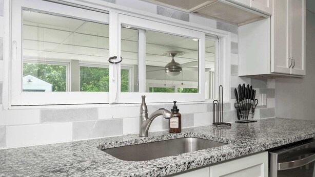 A kitchen with a granite countertop, stainless steel sink, and white cabinets. - Hunley Haven Retreat (Cincinnati)