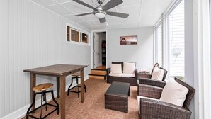 A sunlit room with a ceiling fan, wicker furniture, a wooden table, and a patterned carpet. - Hunley Haven Retreat (Cincinnati)