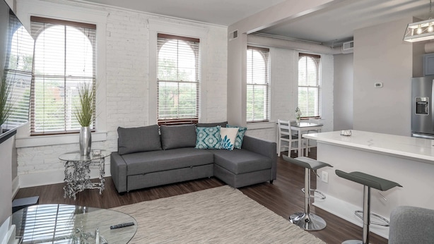 Una sala de estar moderna con un sofá seccional gris, una mesa de centro de vidrio y una zona de bar con taburetes.
