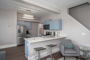 Una cocina moderna con gabinetes grises, electrodomésticos de acero inoxidable y una isla blanca con taburetes de bar.