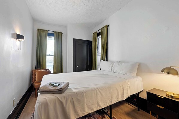 A hotel room with a bed, a chair, a desk, and a lamp.