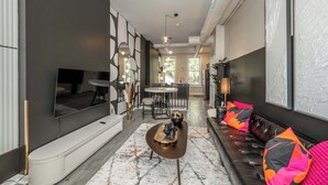 A modern living room with a flat-screen TV, a sofa with colorful cushions, a coffee table, and a dining area with a round table and chairs. - Queen City Views Suites (Cincinnati)