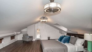 Ein modernes Schlafzimmer im Loft-Stil mit schrägverdeckter Decke, einem großen Bett mit vielen Kissen, einem Sessel und einer Stehlampe.