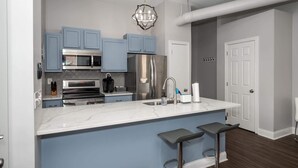 Eine moderne Küche mit blauen Schränken, Edelstahlgeräten, einer Marmorarbeitsplatte und einer Bar mit Barhocker.