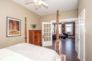 A bedroom with a four-poster bed, a dresser, and a door leading to another room.