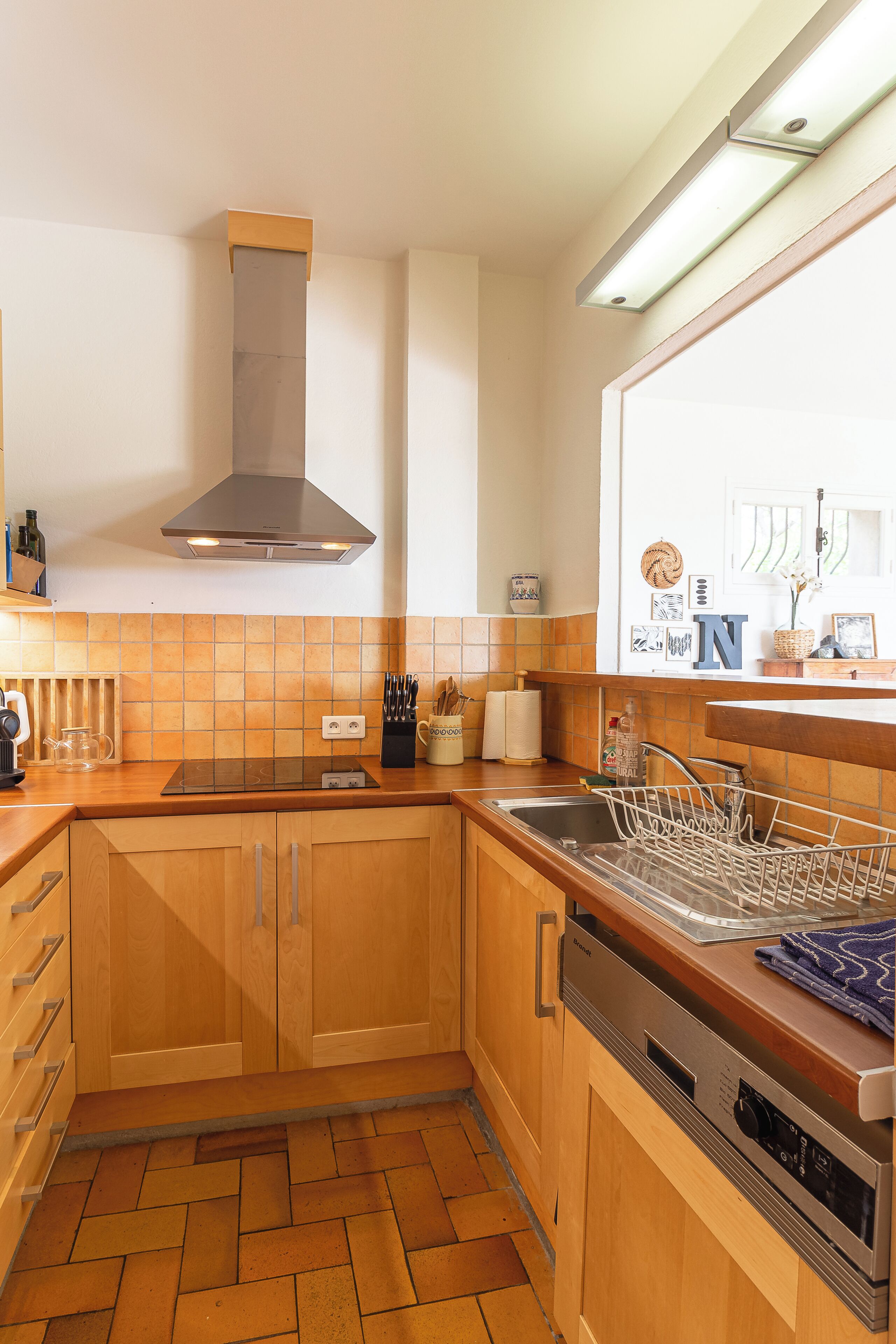 Una cocina compacta con armarios de madera, una campana extractora de acero inoxidable y un lavavajillas.