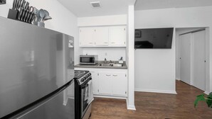 A compact kitchen with white cabinets, a stainless steel refrigerator, a microwave, and an oven. - Northside Suites – 4 Apartments! (Cincinnati)