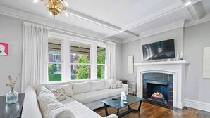A living room with a sectional sofa, a fireplace, a television, and large windows. - Urban Elegance Getaway (Columbus)